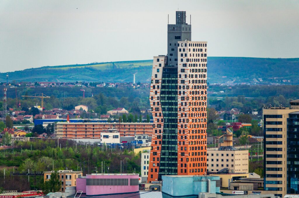 A striking modern skyscraper in Brno with a scenic backdrop of lush hills and contemporary architecture.